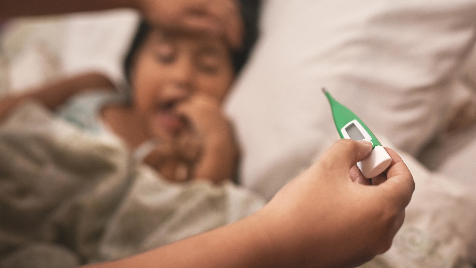 La mÃ¨re d'une enfant couchÃ©e dans un lit prend sa tempÃ©rature Ã  l'aide d'un thermomÃ¨tre.